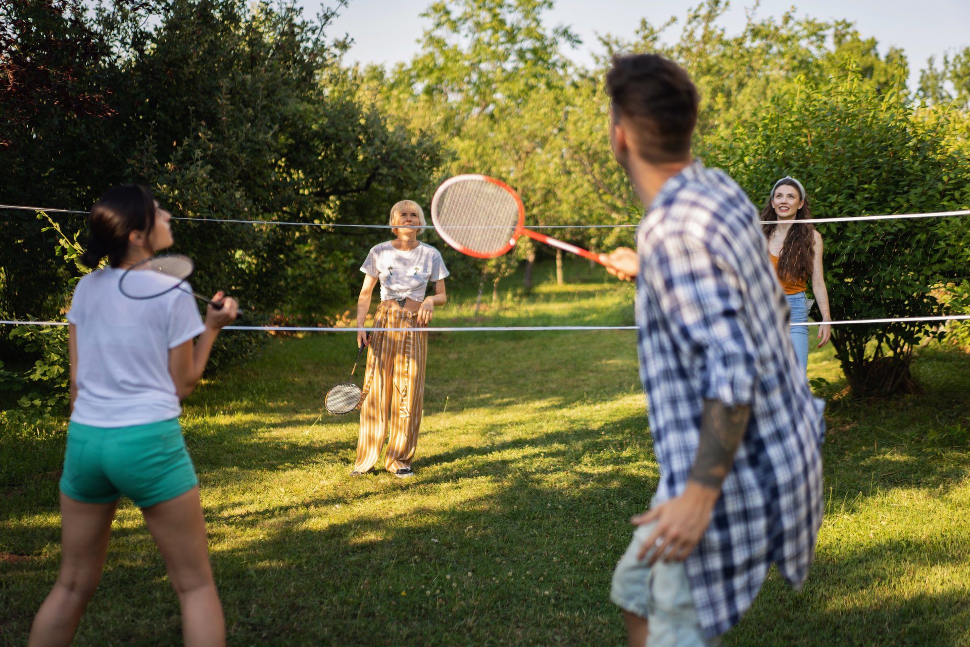 1369805081 Carefree friends playing badminton, during summer day in the garden